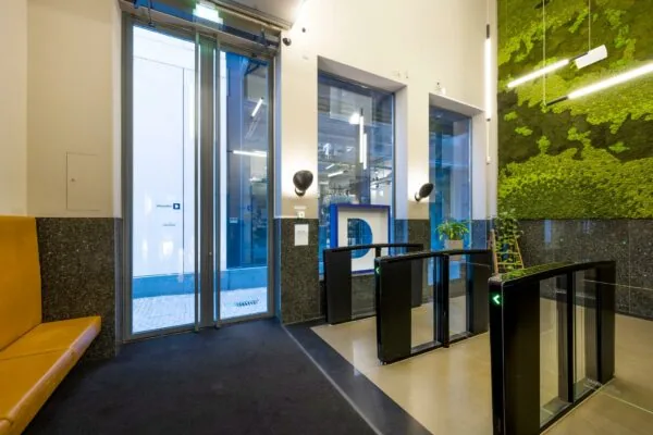 Moderne entreehal van een kantoorgebouw aan de Sint-Jorissteeg met toegangspoortjes, groene moswand en glazen deuren.